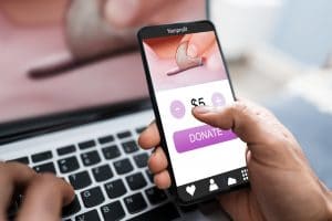 Person donating money on mobile phone while typing on a laptop keyboard with blue background.