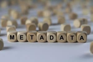 Word metadata spelled out with wooden letter beads on a gray background and more wooden letter beads in the background.